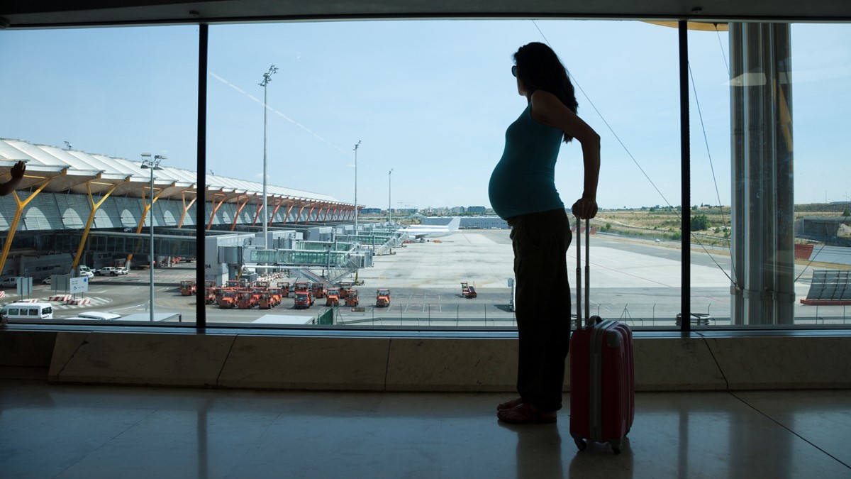 A pregnant woman looks out of the window at an airport.